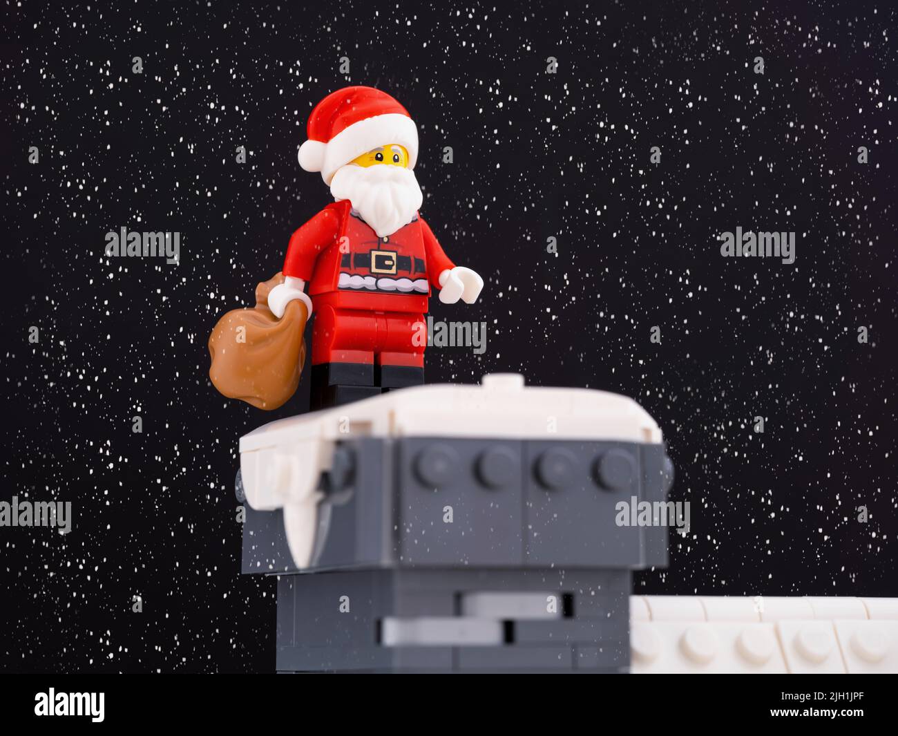 Tambov, Federación Rusa - 26 de mayo de 2022 Un minifigure Lego Santa Claus sosteniendo su bolsa y de pie en una chimenea de la casa mientras nieva . Foto de stock