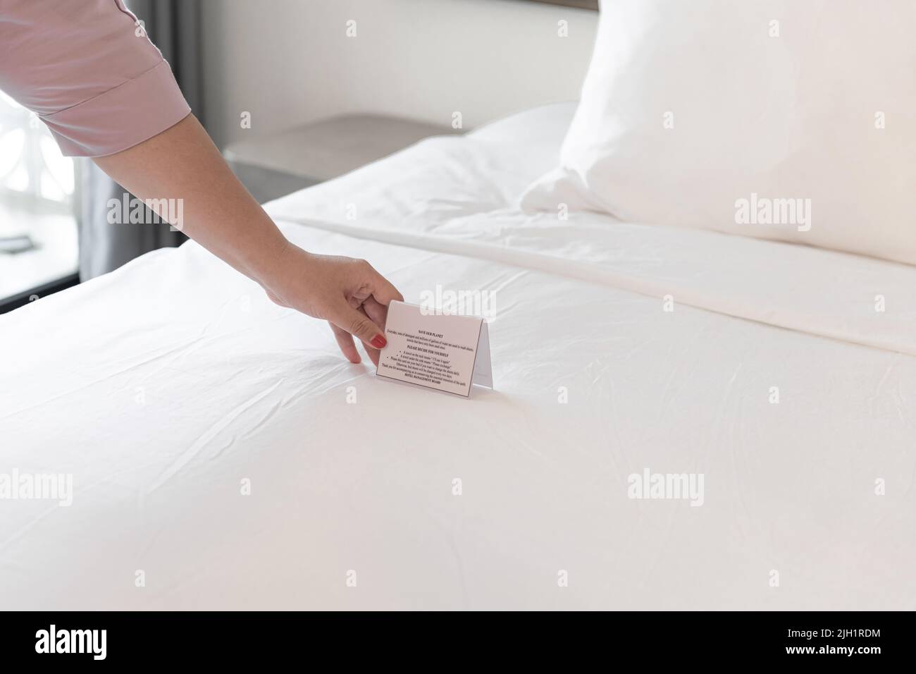La mujer tiene las manos poniendo un cartel para cambiar las sábanas de la cama Foto de stock