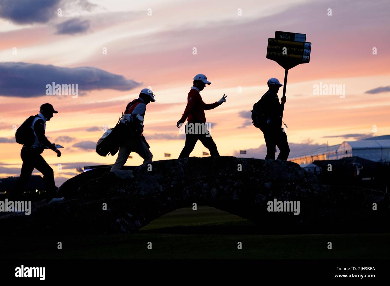 Los jugadores del grupo 51 cruzan el puente Swilcan en poca luz mientras el juego continúa durante el primer día del Open en el Old Course, St Andrews. Fecha de la foto: Jueves 14 de julio de 2022. Foto de stock