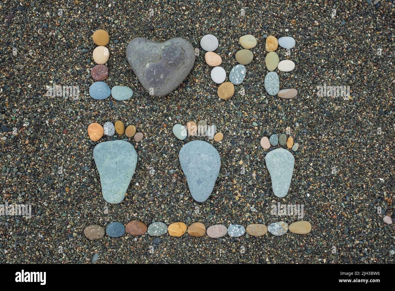 Concepto de amor. Pasos familiares y la palabra amor hecho de piedras en la playa de arena. Foto de stock