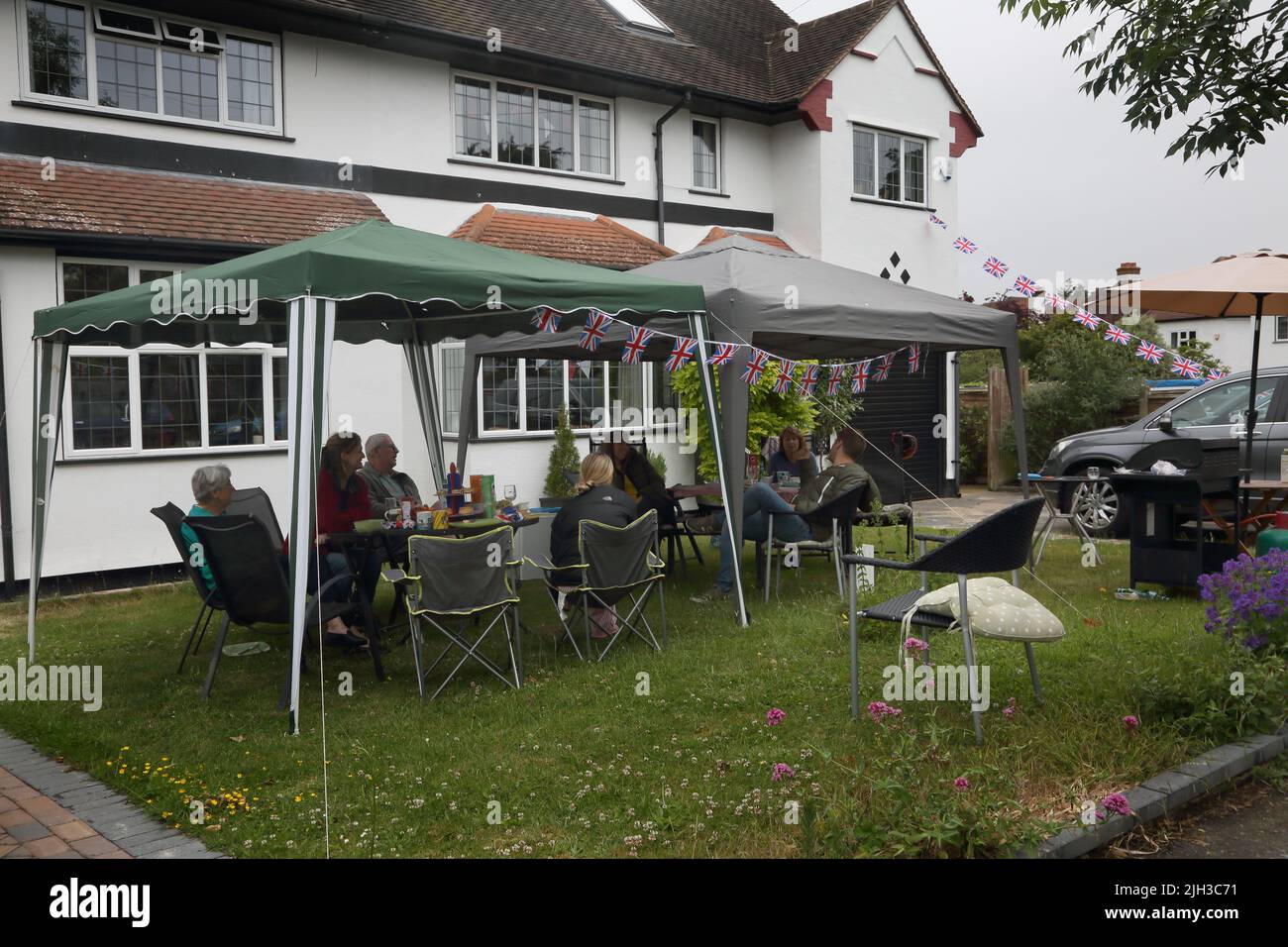 La gente de la fiesta de la calle que se sienta debajo de los cenadores en jardín delantero que celebra reina Elizabeth II Platinum Jubilee Surrey Inglaterra Foto de stock