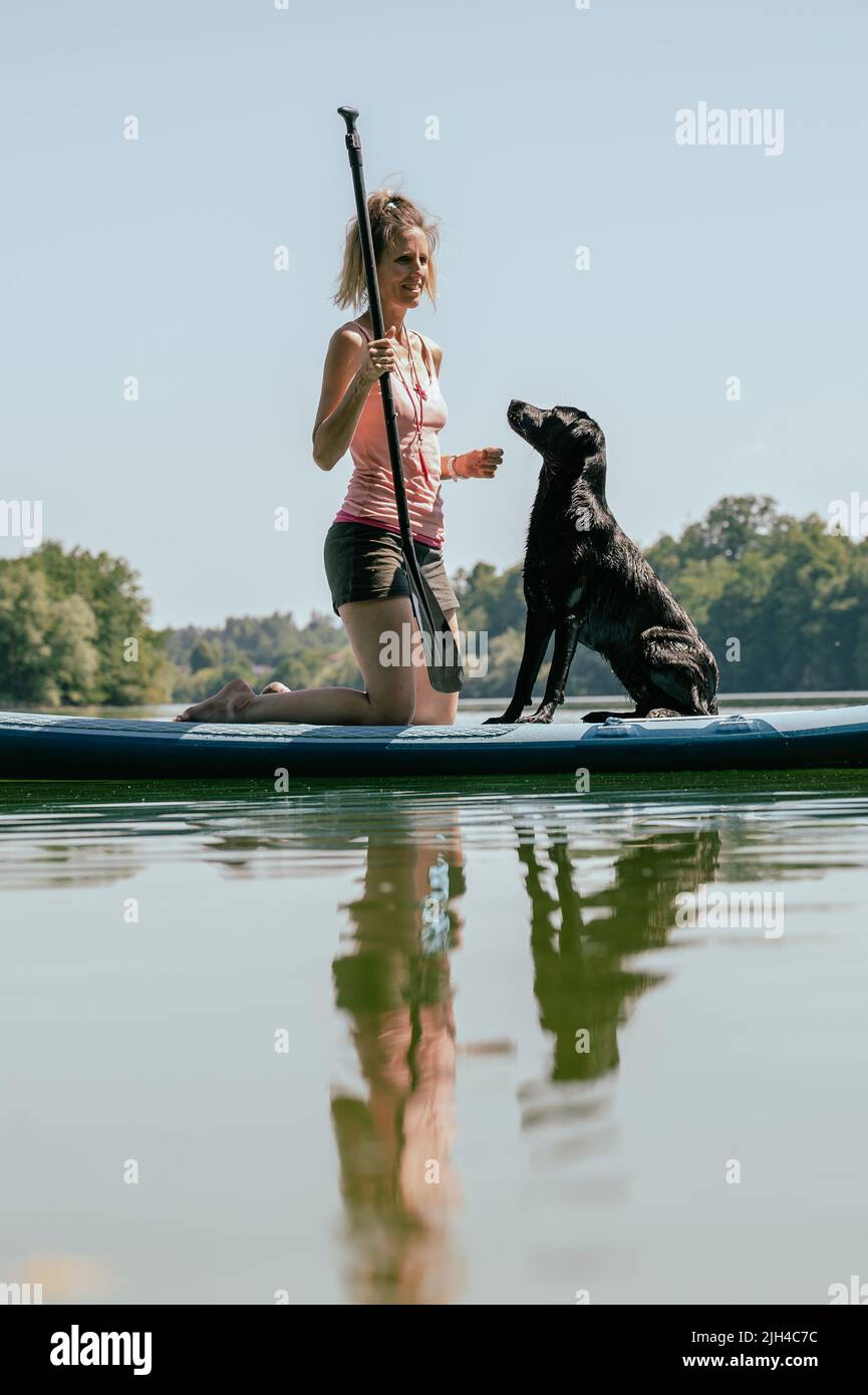 Joven dueña de perro y su perro labrador negro retriever en una tabla en el río. Foto de stock