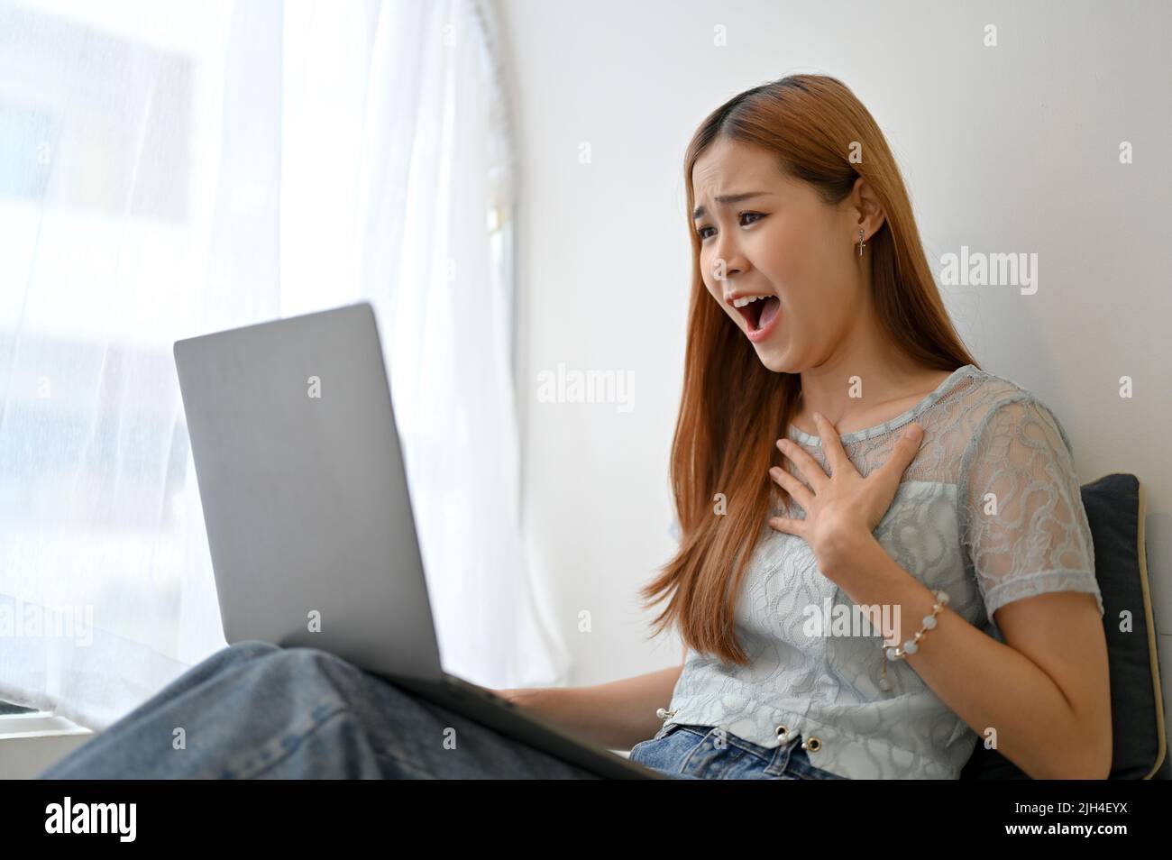 Mujer asiática joven asombrada y excitado recibiendo noticias inesperadas, un email de la oferta del trabajo, una promoción del trabajo, o ganando la lotería a través de su computadora portátil Foto de stock