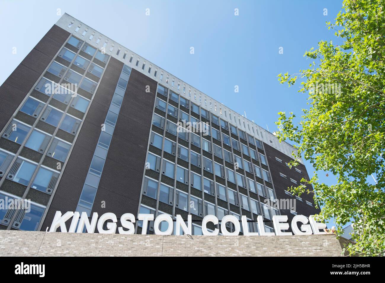 exterior de kingston college, una universidad de educación adicional en kingston upon thames, surrey, inglaterra, con un trabajador en casco sólo visible por un cartel Foto de stock