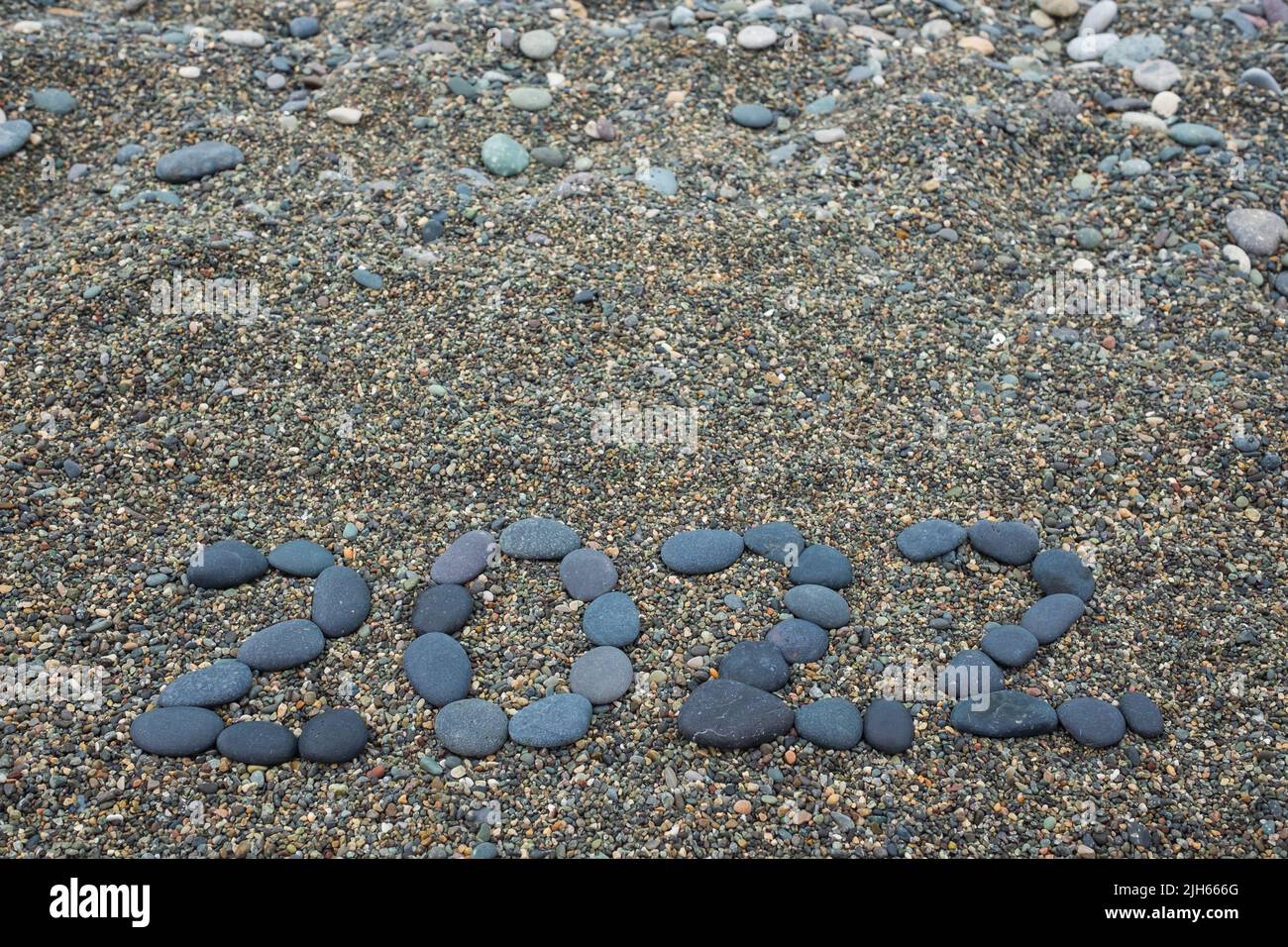 Año 2022 Hecho de piedras negras en la playa de arena. Mal concepto de año Foto de stock