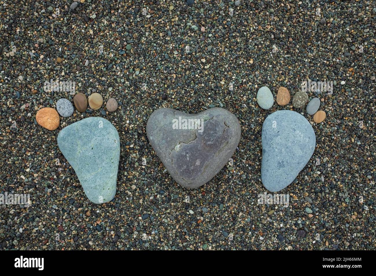 Concepto de amor. Pasos de hombre, mujer y corazón hechos de piedras en la playa de arena. Foto de stock