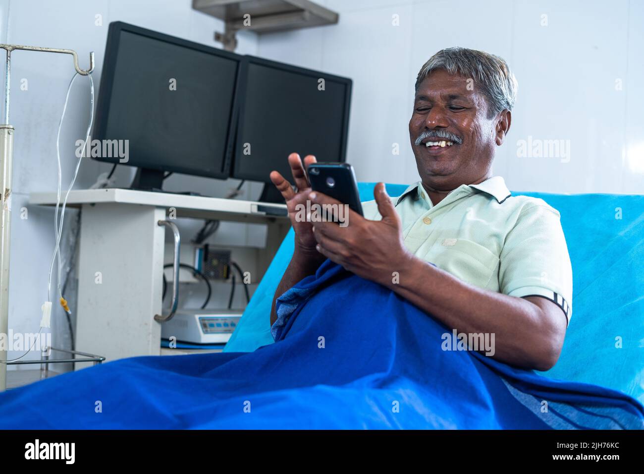 Anciano sonriente y feliz usando el teléfono móvil en el hospital mientras se acuesta en la cama - concepto de tratamiento medicare, redes sociales y relajación Foto de stock