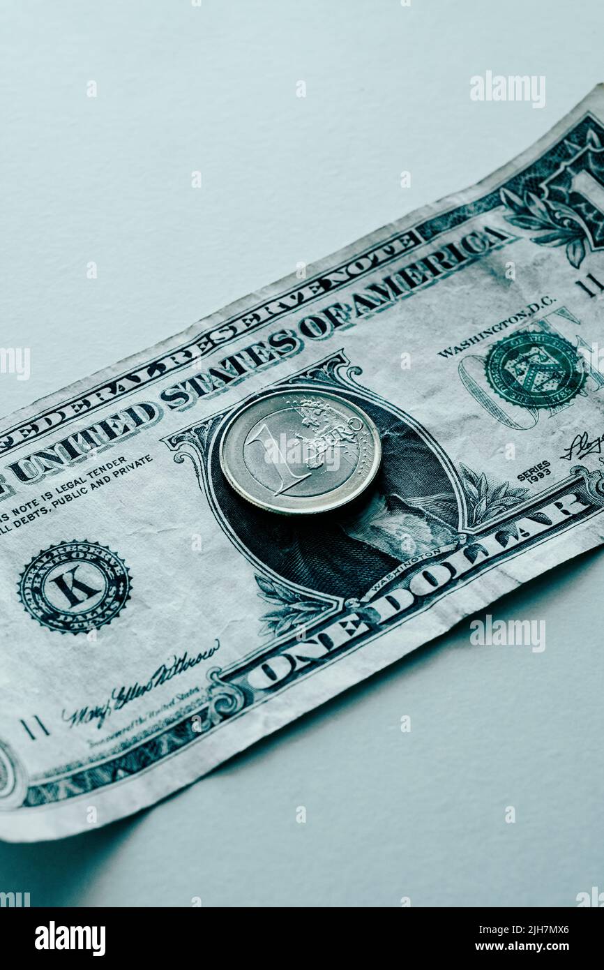 Primer plano de una moneda de 1 euros y un billete de 1 dólares en una superficie blanca, que representa la casi paridad entre las dos monedas Foto de stock