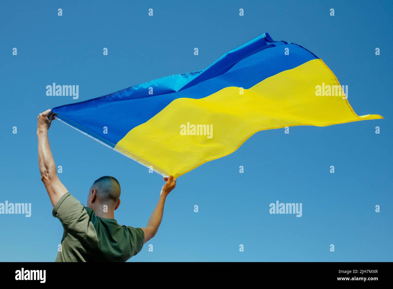 primer plano de un hombre, visto desde atrás, ondeando la bandera ucraniana en el cielo sobre su cabeza, en un día soleado Foto de stock