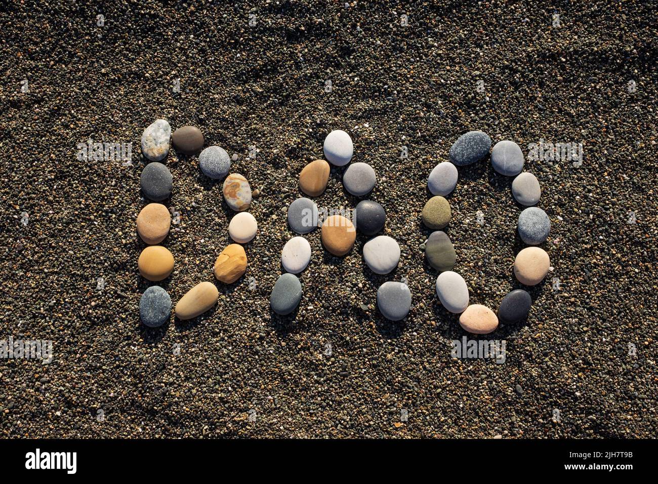 Organización autónoma descentralizada. Puzzle, palabra DAO hecho de piedra en la playa de arena. Foto de stock