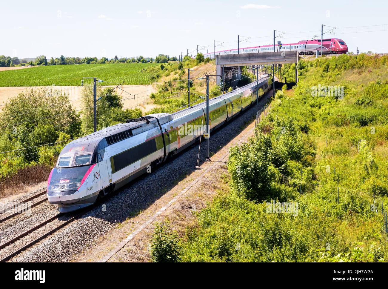 Un TGV Inoui y un tren de alta velocidad Thalys pasan uno sobre otro en el campo en un día soleado. Foto de stock