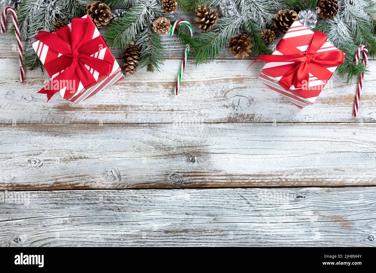Concepto de vacaciones de Navidad y Año Nuevo con ramas de abeto cubiertas de nieve, cajas de regalo de rayas tradicionales, bastones de caramelo y conos de pino dorado plateado en blanco Foto de stock