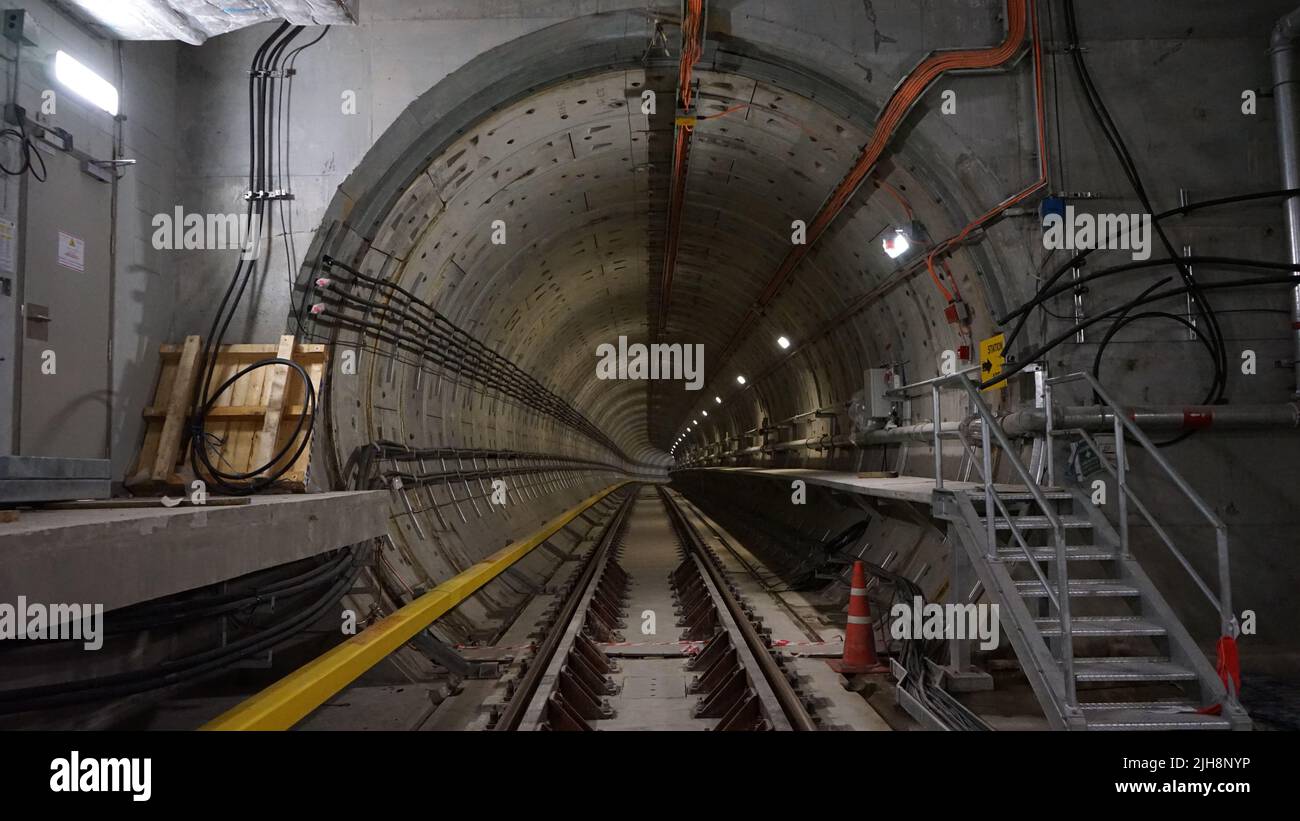 Un túnel de hormigón con ferrocarril y cables eléctricos, escalera de metal y luces Foto de stock