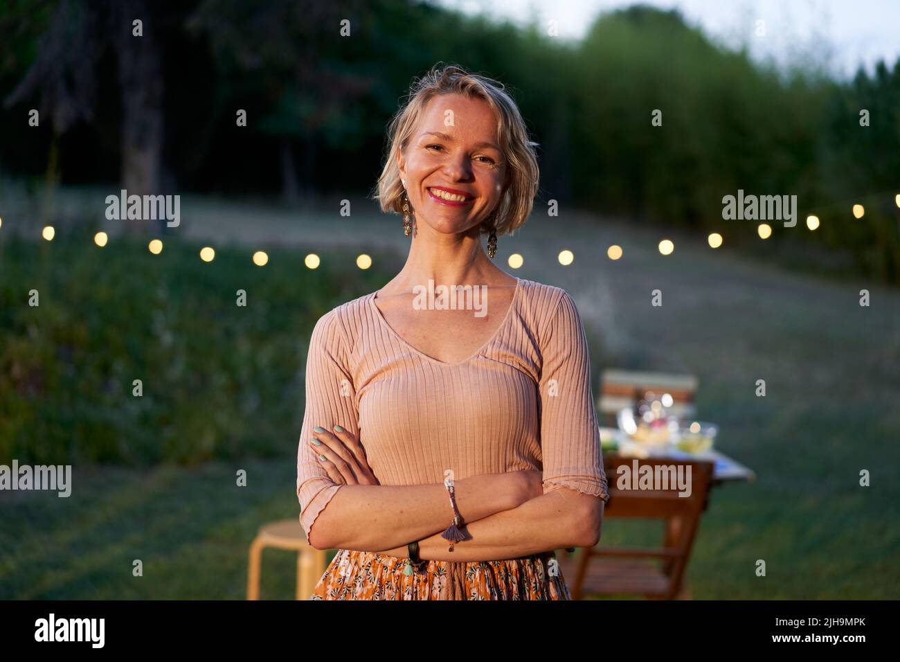 Retrato de una mujer escandinava rubia de mediana edad mirando la cámara. Mujer nórdica sonriente en el patio trasero o en un restaurante. Foto de stock