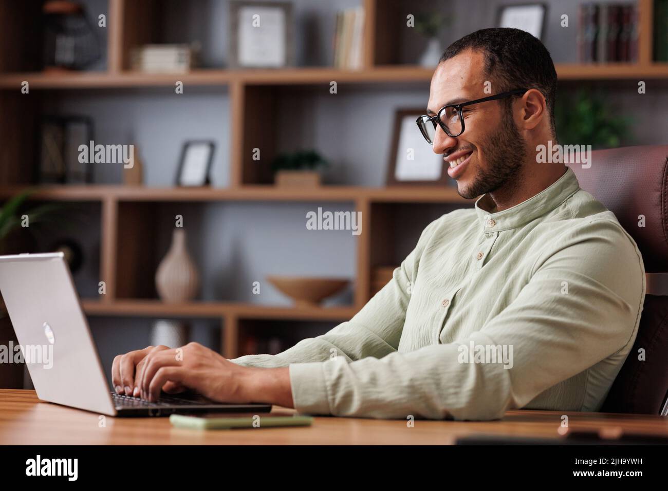 Retrato de un joven hombre de negocios africano que trabaja con un ordenador portátil en la oficina. Sonriente empresario confidente usando gafas con computadora en Foto de stock