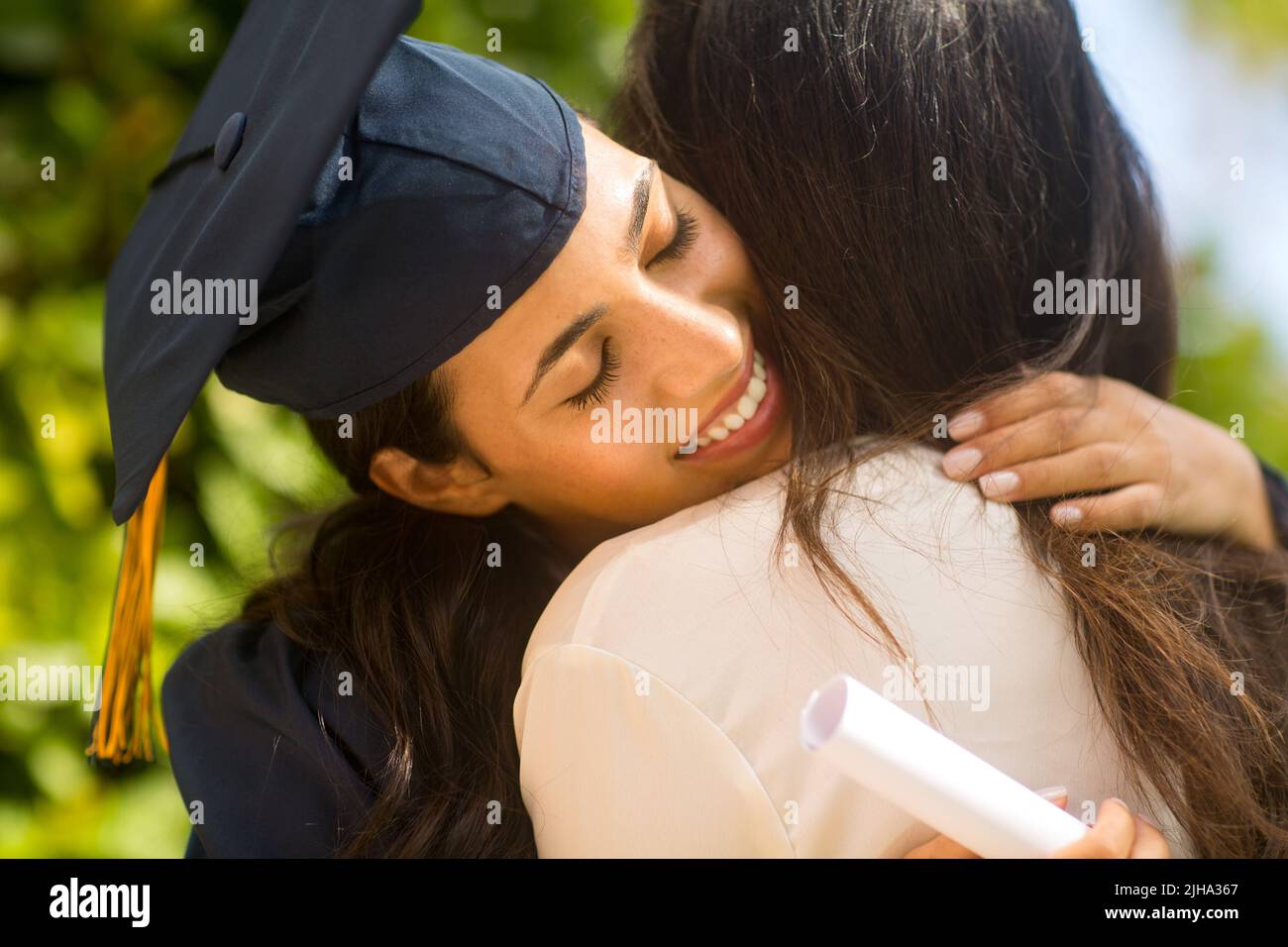 Madre orgullosa abrazando a su hija en su graduación Foto de stock