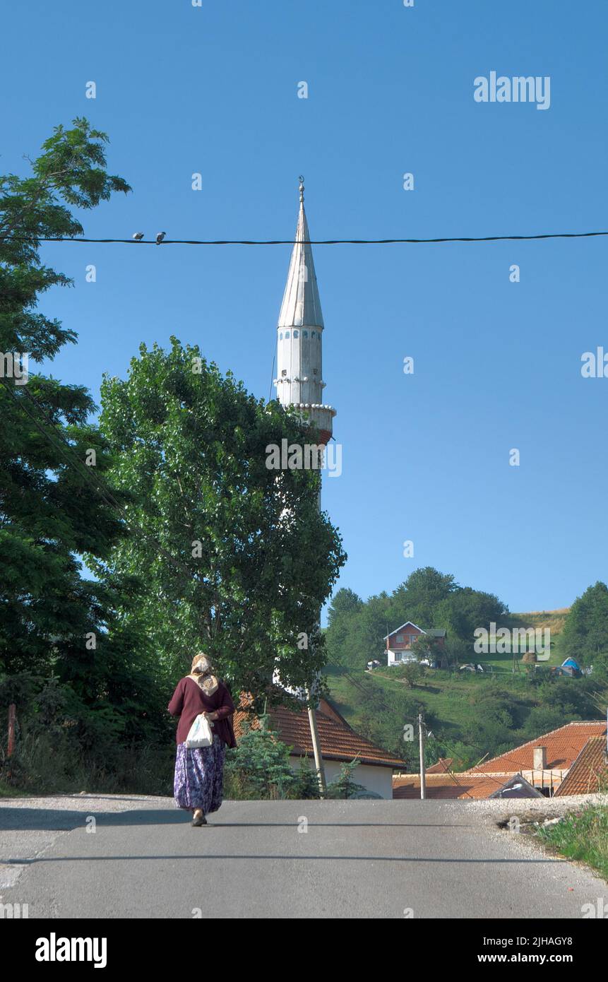 Mujer musulmana vestida de forma tradicional caminando por la carretera que conduce a la mezquita de la aldea de Serbia Foto de stock