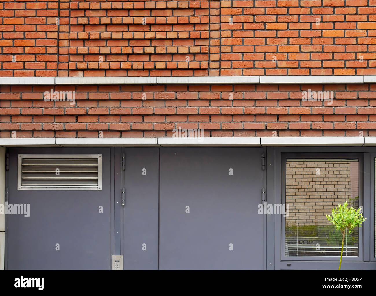 Elevación de forma geométrica de la pared exterior de ladrillo con puerta metálica, edificio de diseño moderno Foto de stock