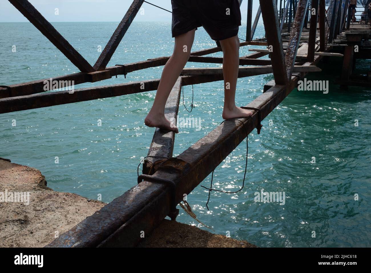 Hombre yendo y equilibrando en un puente roto sobre el río o el mar. Vista en agujero y agua azul Foto de stock