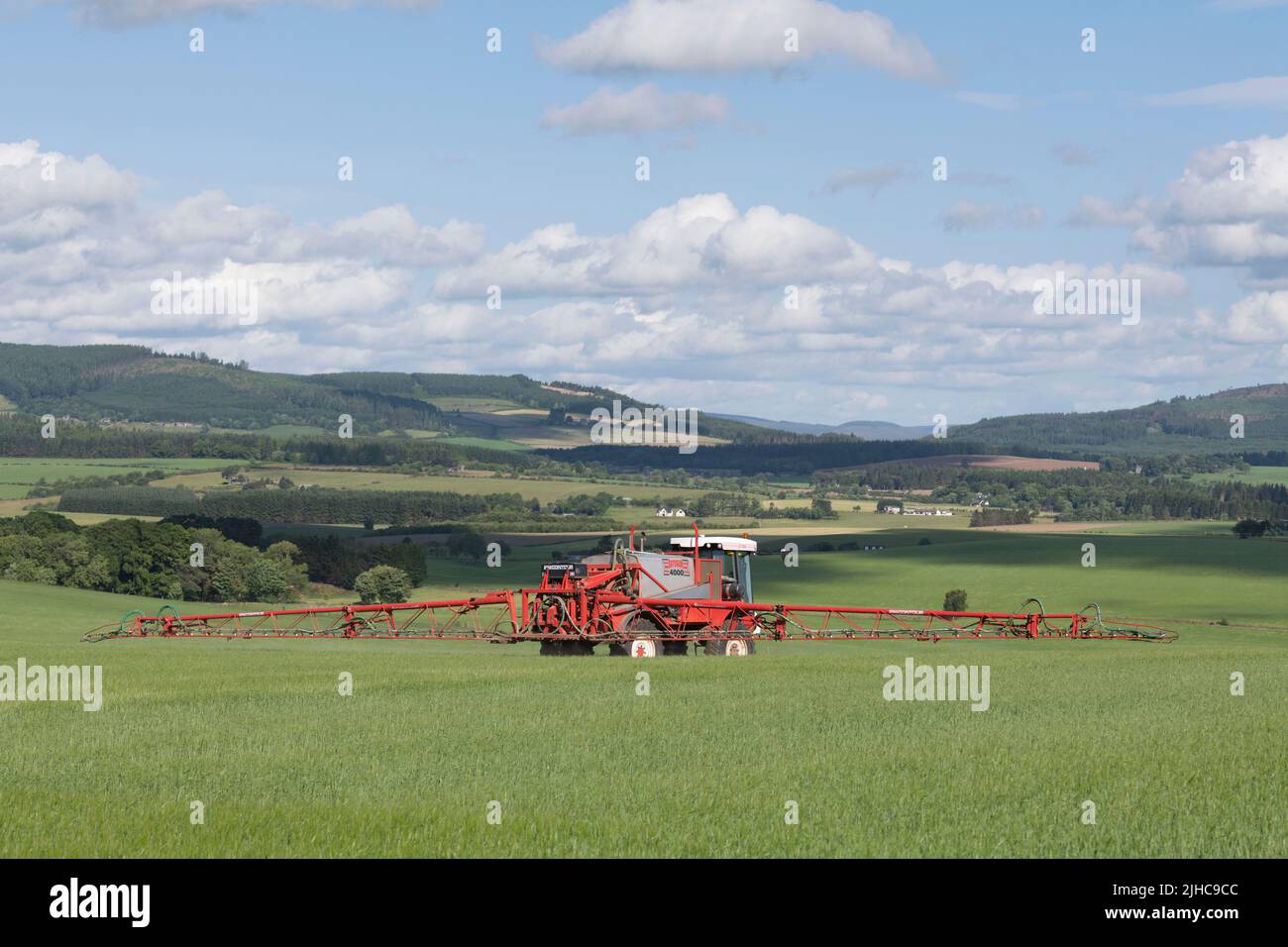 Un Bateman 4000 rociando un campo de cebada en verano Sunshine con vistas a Un paisaje escénico en Aberdeenshire Foto de stock