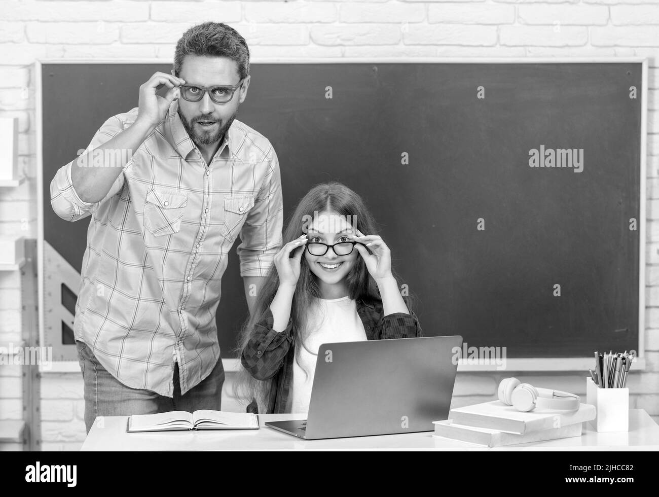 niño y papá asombrados sentados en el salón de clases con computadora en pizarra, e-learning Foto de stock