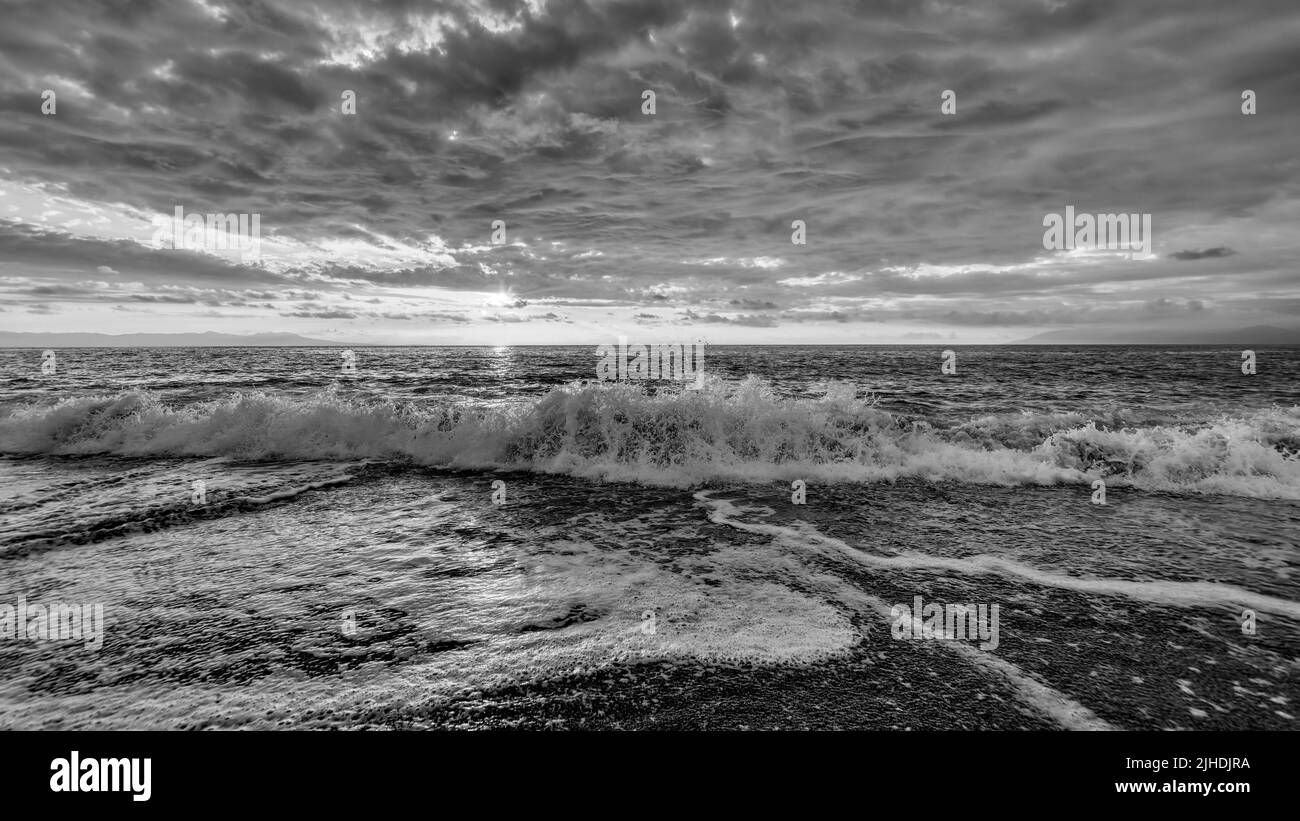 Una ola del océano se está rompiendo con nubes en blanco y negro Foto de stock