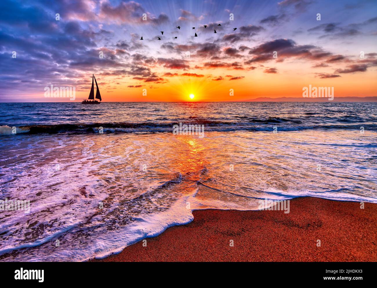 Los rayos del sol están estallando en el amanecer del horizonte del océano con un velero que vela y pájaros que vuelan sobre arriba Foto de stock