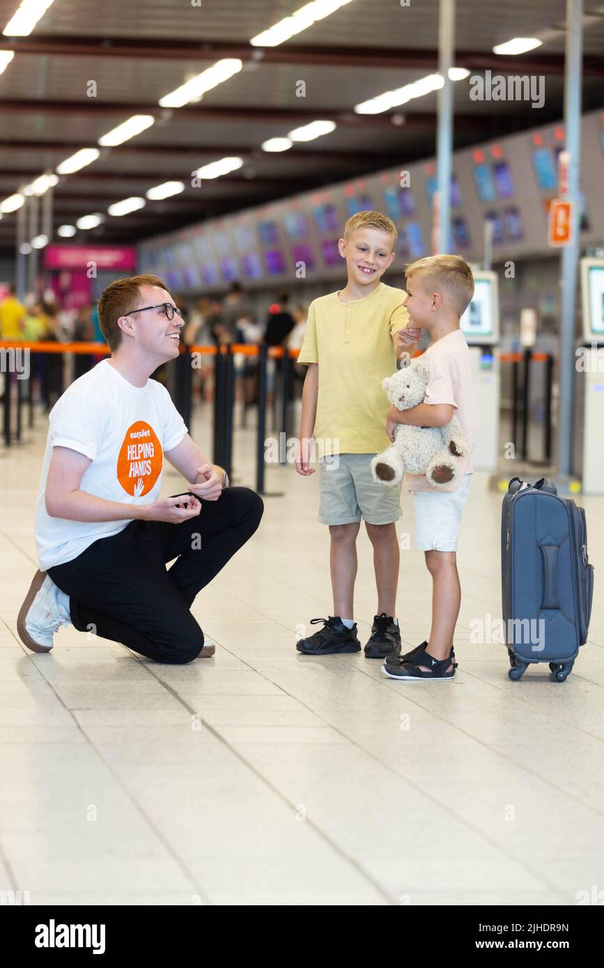 Callum Whyman, asistente de atención al cliente de easyJet, ayuda a una familia joven en el aeropuerto de Luton mientras la aerolínea lanza su nueva línea de atención al cliente familiar. Fecha de emisión: Lunes 18 de julio de 2022. Foto de stock