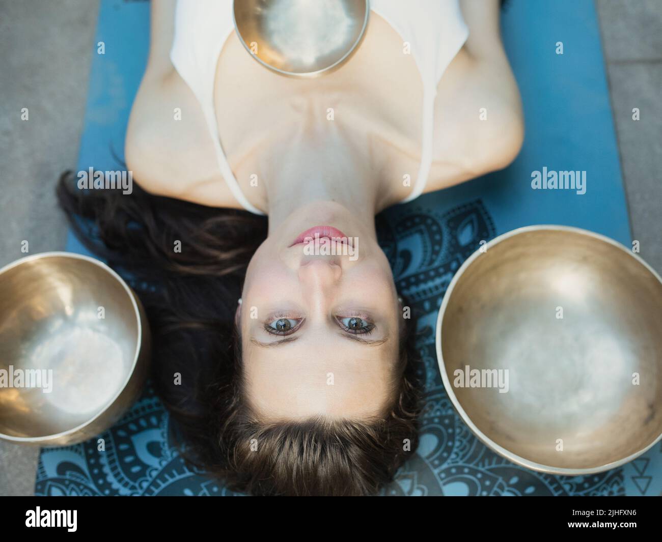 Concepto de yoga, meditación y terapia de sonido. Retrato de la hermosa joven mujer caucásica rodeada de tazones e instrumentos tibetanos de canto de cobre Foto de stock