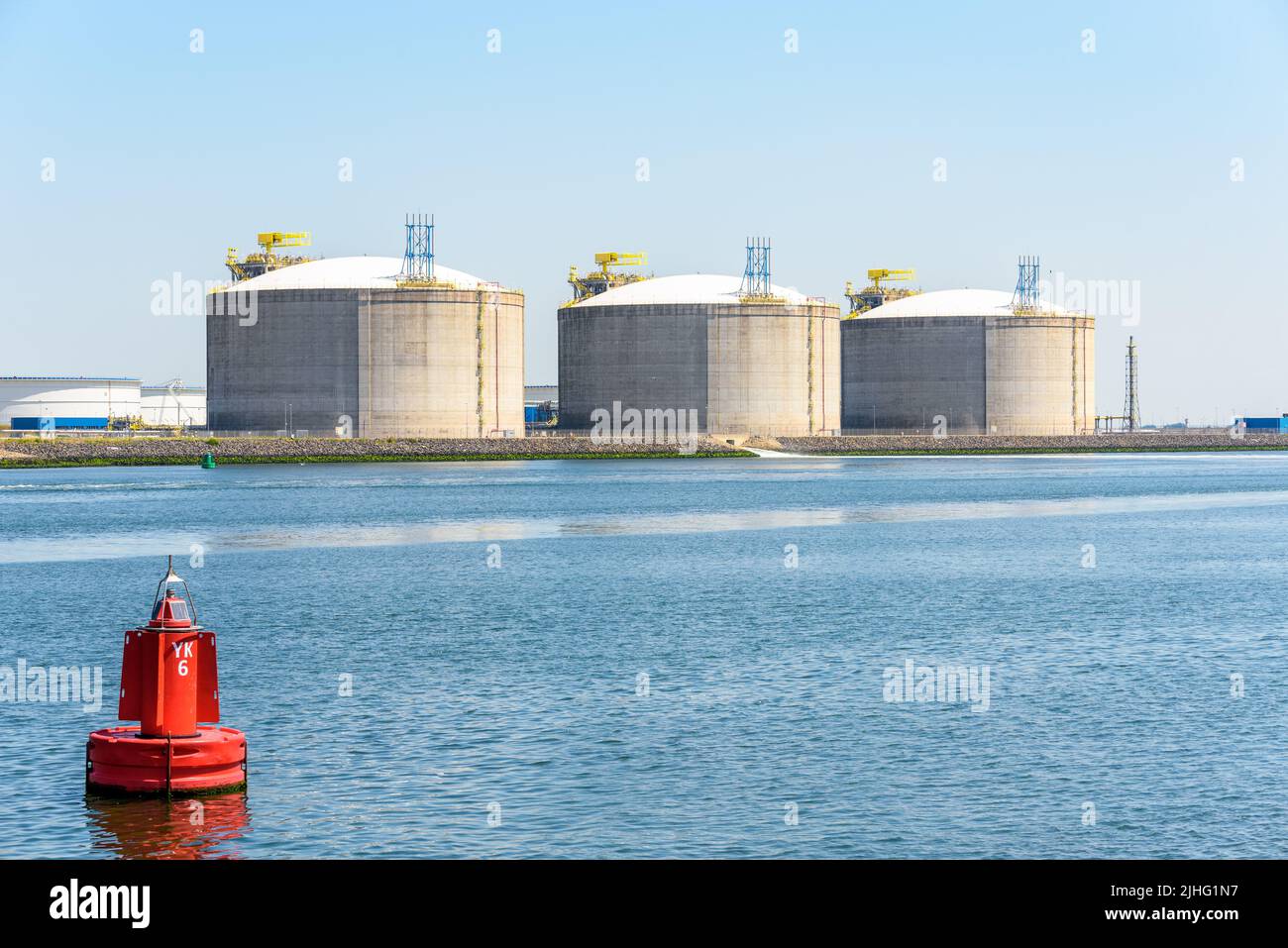 Terminal de gas natural licuado con grandes tanques de hormigón a lo largo de un puerto en un día soleado Foto de stock