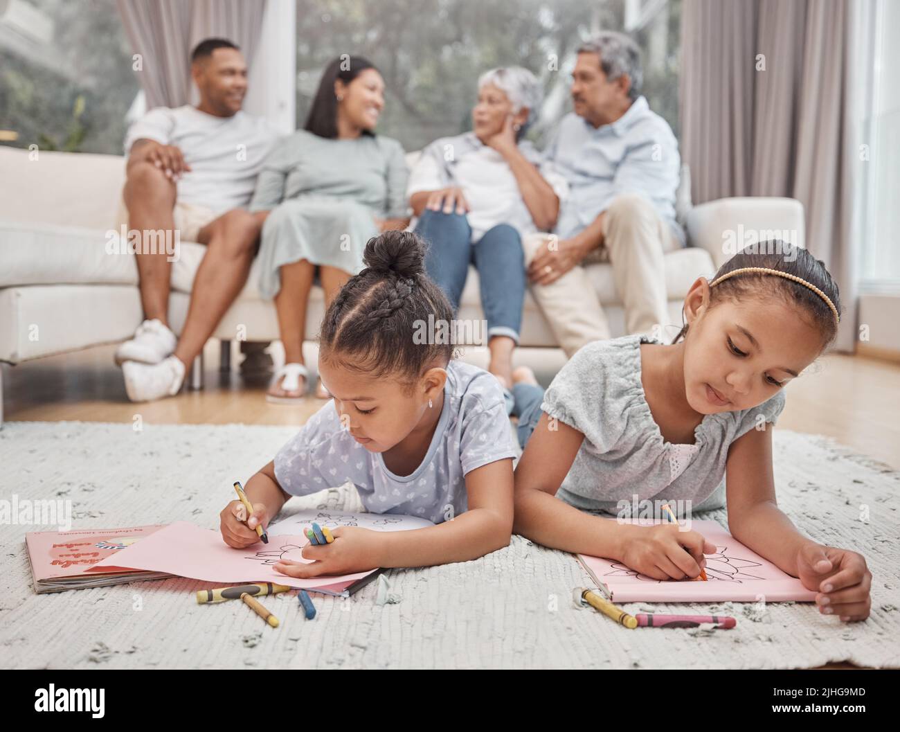 Dos lindas hermanas hermanas de raza mixta dibujando y coloreando en la sala de estar con sus padres y abuelos en el fondo. Niños sin preocupaciones Foto de stock