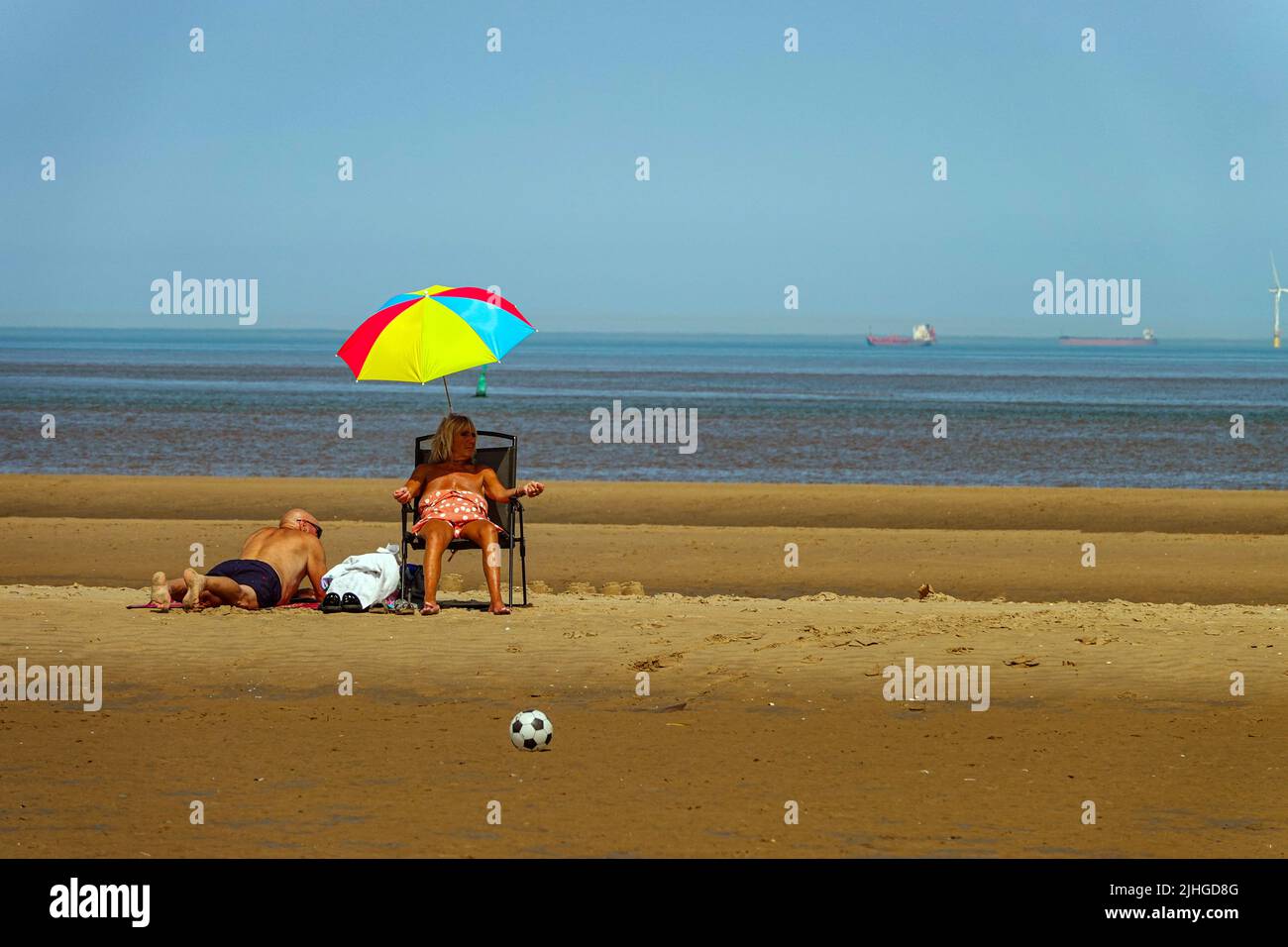 Gente mayor bajo la sombrilla de la playa, el día más caluroso en el Reino Unido en Talacre Beach, y el faro Point of Ayr, Flintshire, Gales del Norte Foto de stock