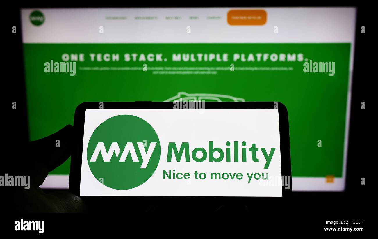 Persona que sostiene el teléfono móvil con el logotipo de la compañía de conducción autónoma de EE.UU. May Mobility Inc. En la pantalla delante de la página web. Enfoque la pantalla del teléfono. Foto de stock