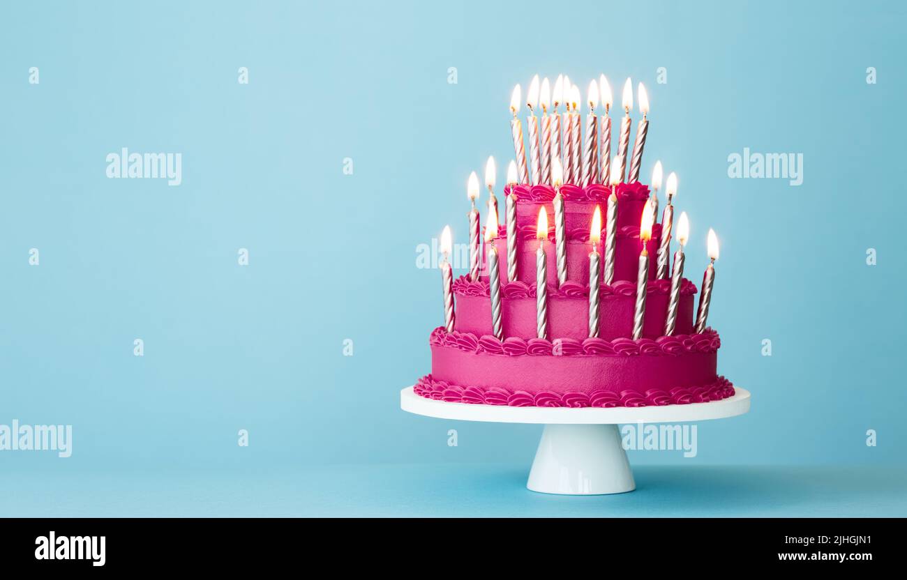 Extravagante pastel de cumpleaños escalonado rosa con muchas velas de cumpleaños doradas sobre un fondo azul Foto de stock
