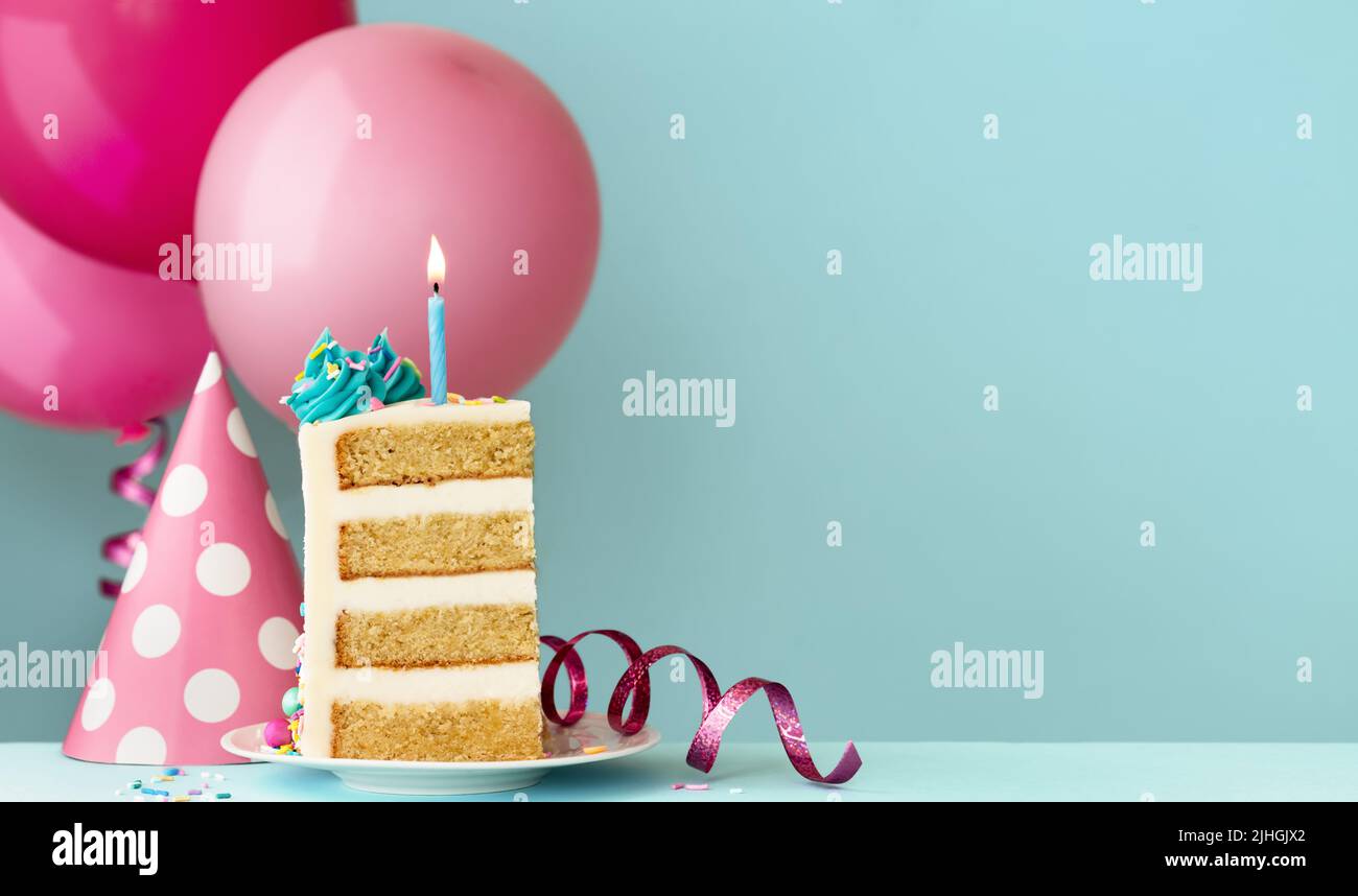 Una rebanada de pastel de cumpleaños con vela azul de cumpleaños, sombrero de fiesta, streamers y globos de cumpleaños listos para una fiesta de cumpleaños Foto de stock