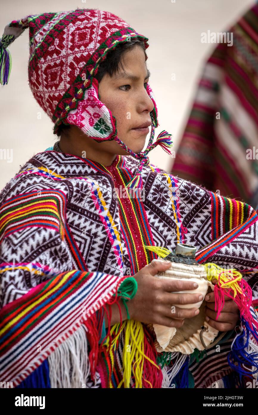 Niño quechua sosteniendo un caracol y vestido con traje tradicional fuera de la iglesia, Pisac, Cusco, Perú Foto de stock