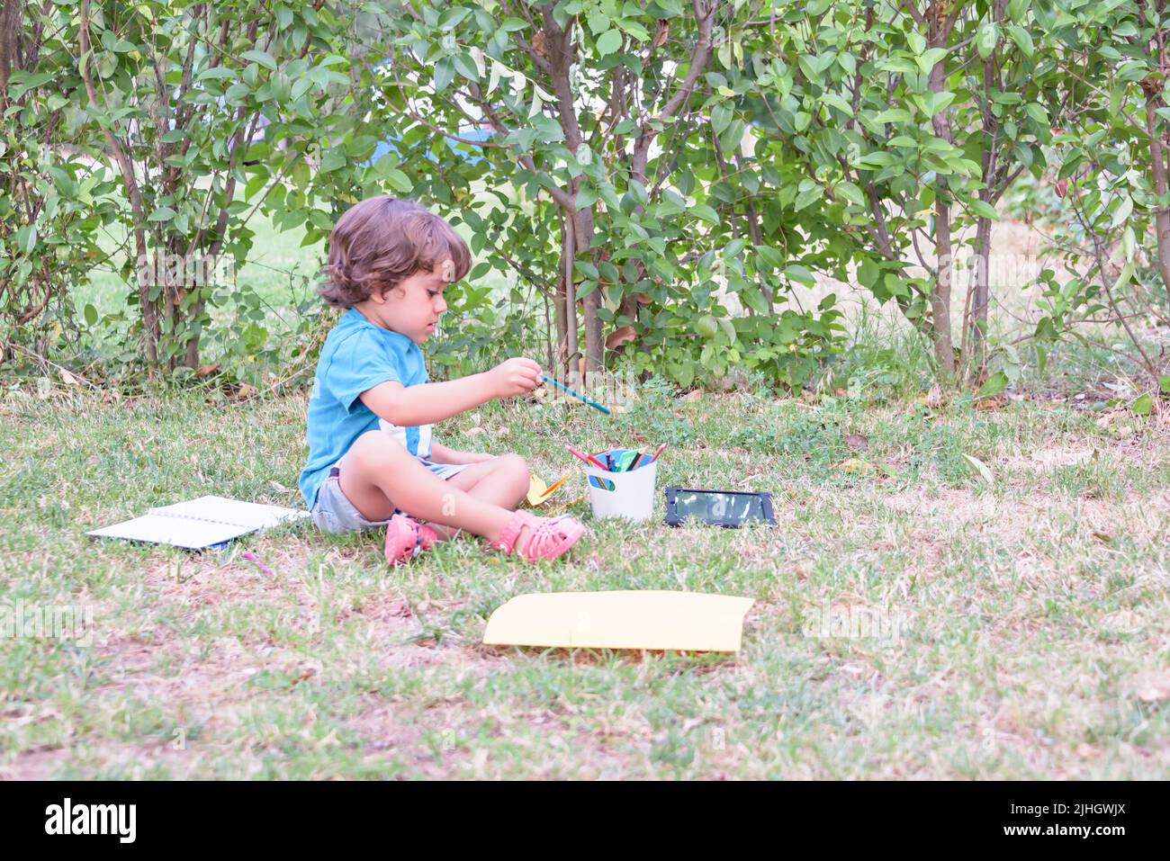 El niño está usando un bolígrafo mágico para dibujar en un libro sobre una mesa de madera en el parque con expresión facial de determinación. Foto de stock