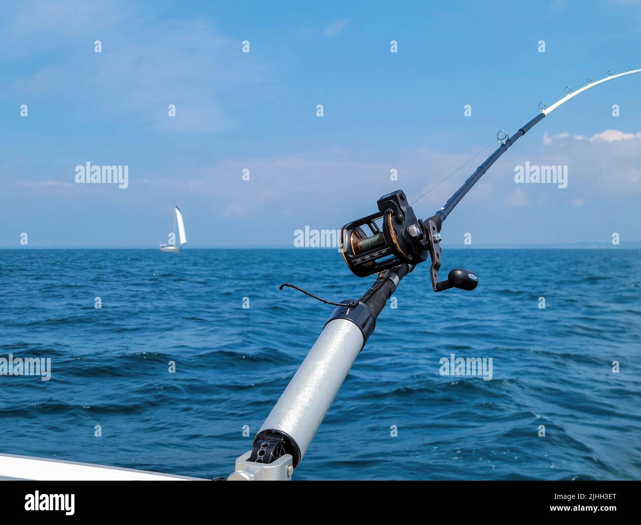 Caña de pescar en portacañas con velero en el fondo Foto de stock