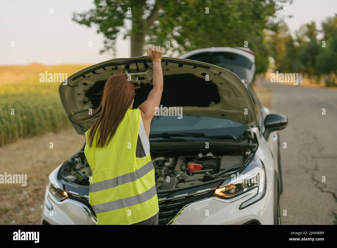 vista trasera de una mujer con un chaleco reflectante que abre el capó de su coche Foto de stock