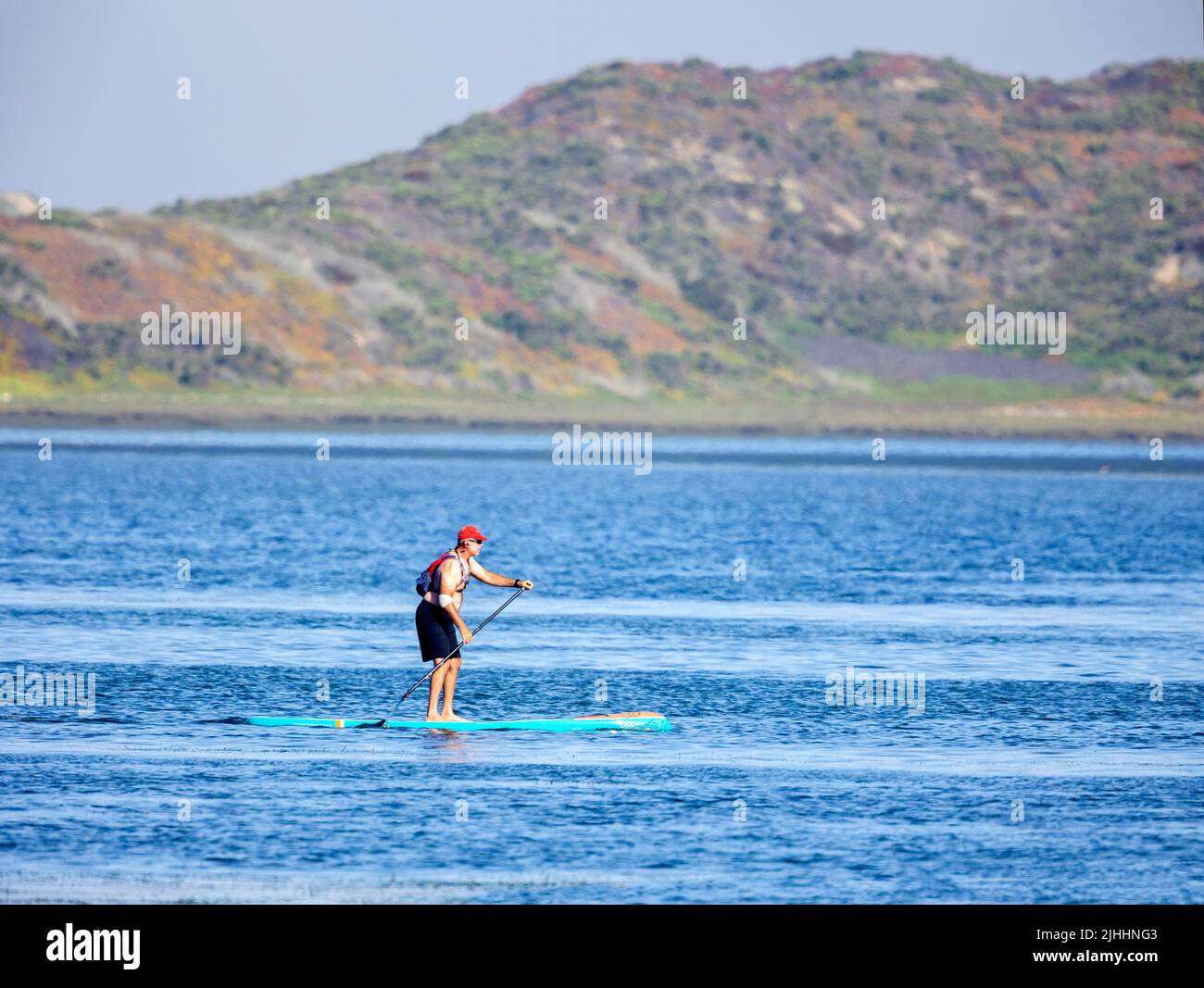 Hombre con gorra roja Paddleboarding en Morro Bay Foto de stock
