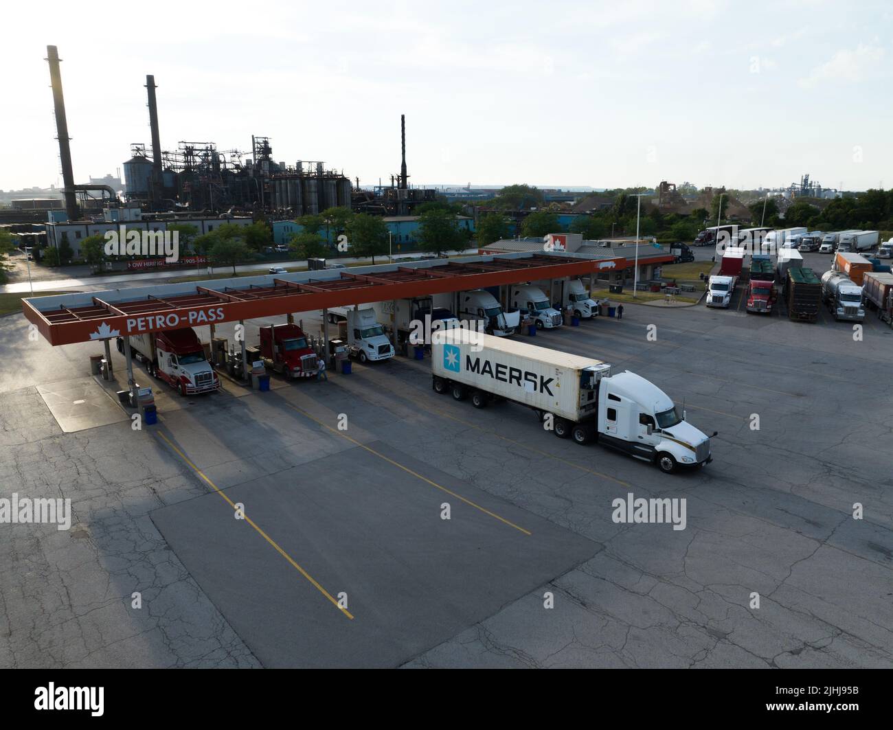 Un contenedor Maersk en un camión de transporte sale de una gran gasolinera en un sector industrial en una tarde soleada. Foto de stock
