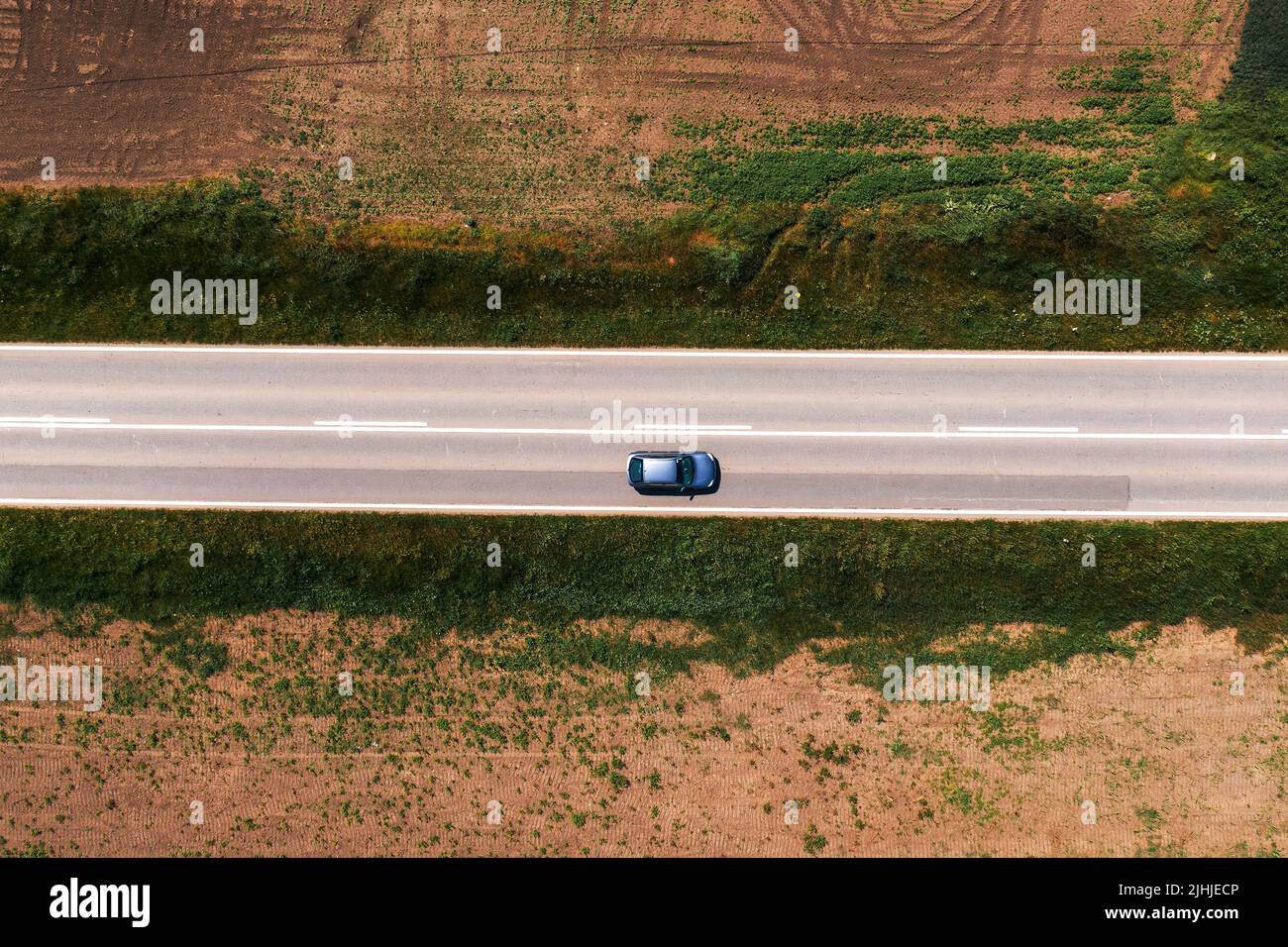 Foto aérea de coche de pasajeros conduciendo a lo largo de carretera asfaltada a través de paisaje rural sin árboles y sombra en la tarde de verano caliente y soleado, drone pov Foto de stock