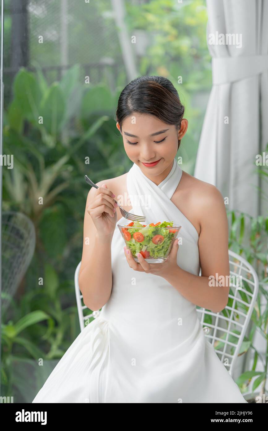 Una mujer sana de estilo de vida comiendo ensalada sonriendo feliz en el interior en un hermoso día Foto de stock