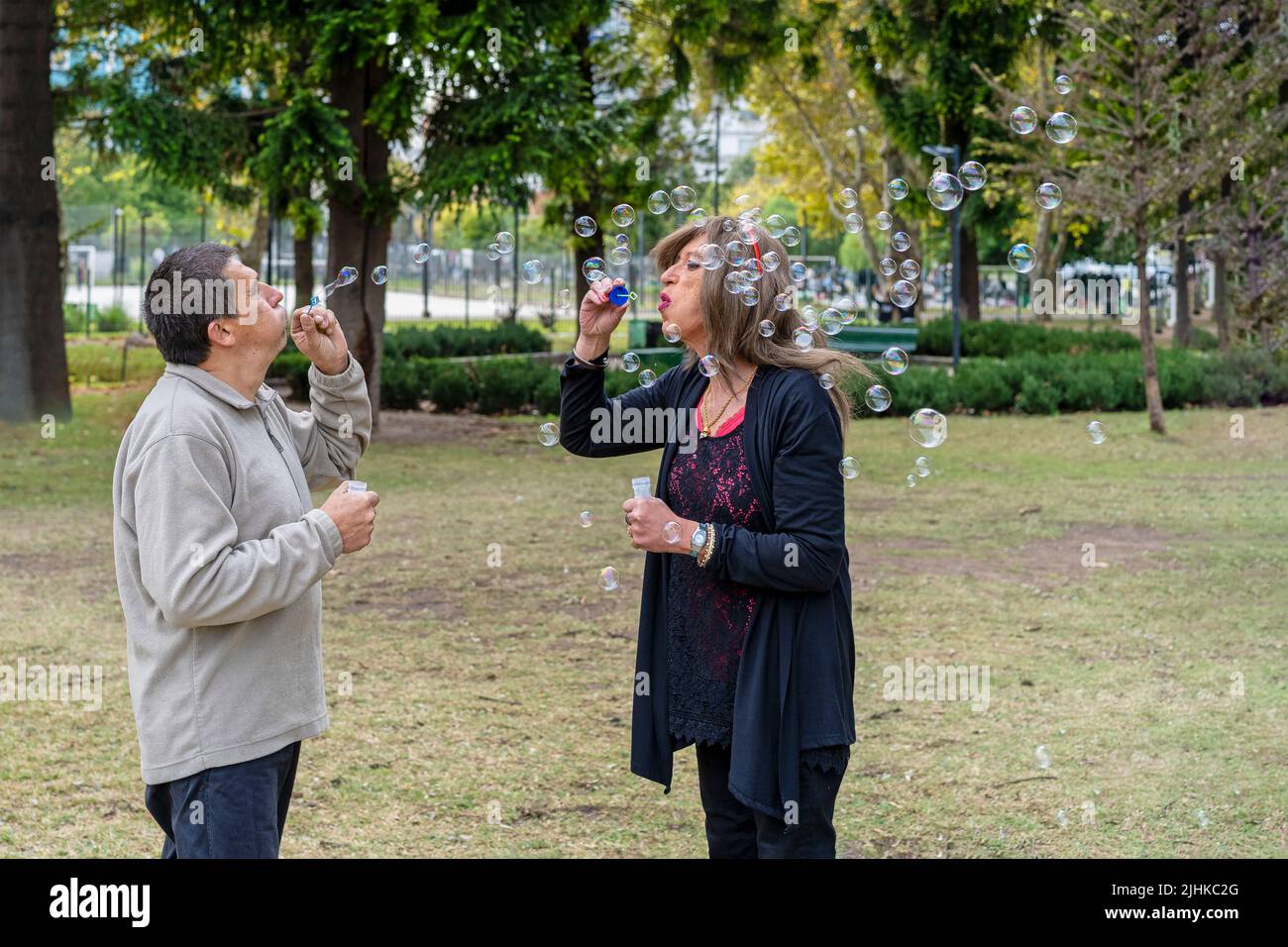 Alegre pareja de queer maduro soplando burbujas en un parque Foto de stock