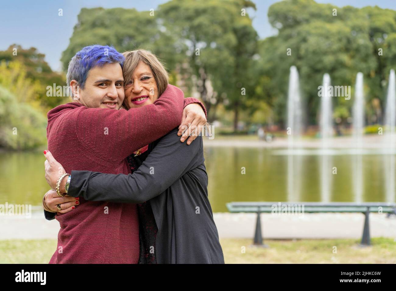 Alegre pareja queer abrazando en un parque mirando la cámara Foto de stock