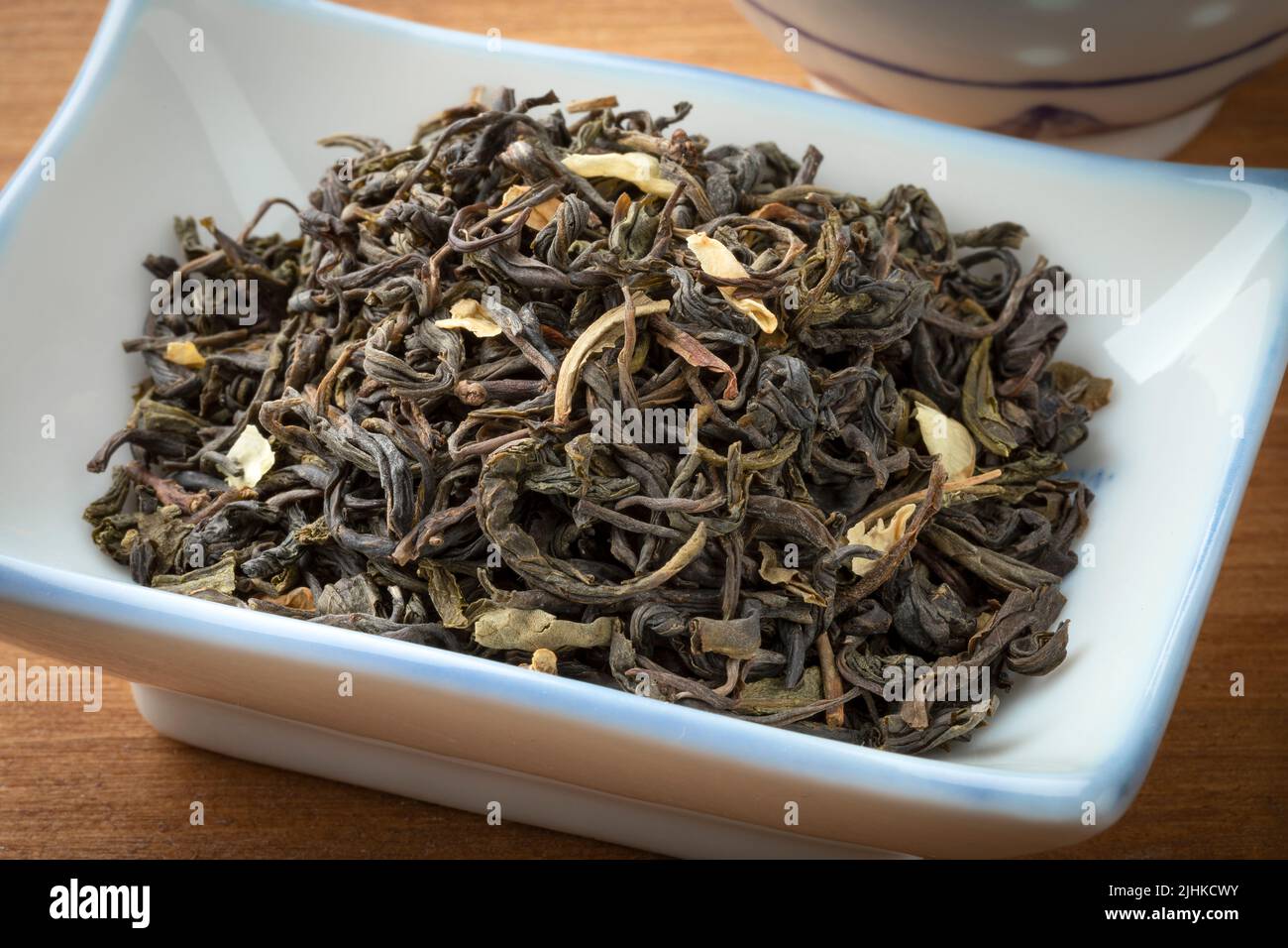 El té de jazmín chino seco deja de cerca en un cuenco sobre un fondo de madera Foto de stock