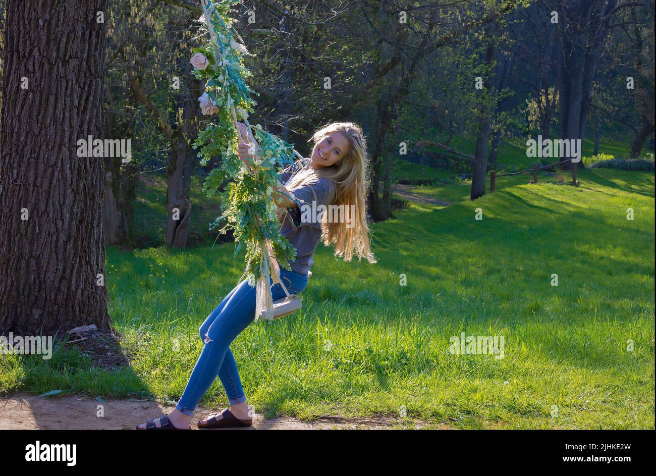 Una mujer joven disfruta balanceándose en un columpio al aire libre decorado con flores. Foto de stock