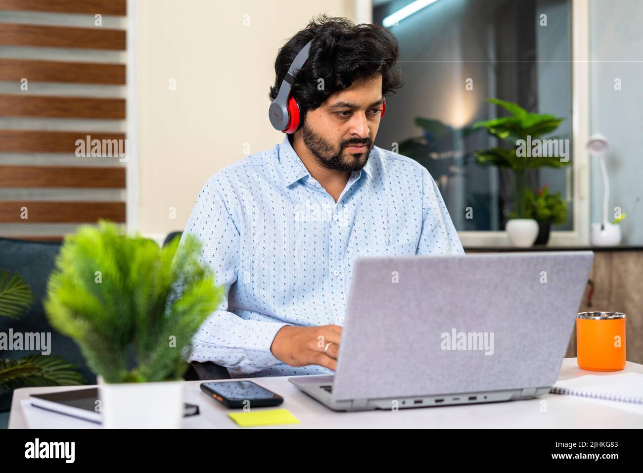 Joven con auriculares inalámbricos trabajando en el portátil mientras está sentado en la oficina: Concepto de reunión en línea, estilo de vida laboral y empleo Foto de stock