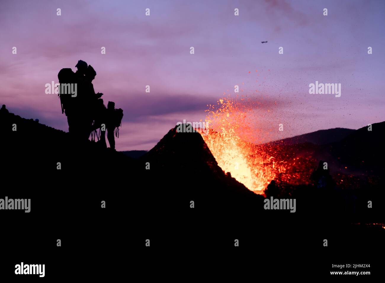 Shilouettes negras de turistas viendo una erupción en islandia al anochecer Foto de stock