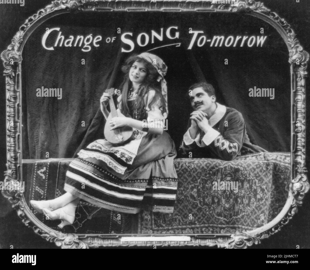 Cambio de canción mañana - La foto muestra a una mujer tocando un instrumento musical mientras un hombre la admira. Impresión en papel positiva de una diapositiva de linterna utilizada en las salas de cine como anuncio. Foto de stock